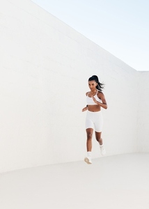 Full length of a young slim female sprinting in a white outdoor studio
