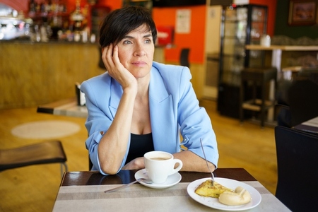 Pensive female with cup of coffee and breakfast in cafe