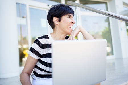Delighted adult woman using laptop on street