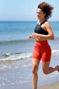 Smiling sportswoman running on sandy beach near seawater