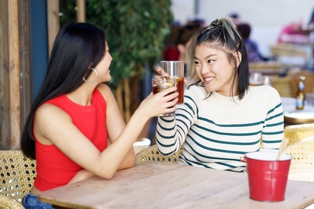 Joyful Asian women clinking glasses of cold tea in cafe