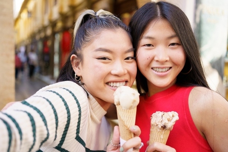 Two young Chinese girls taking a selfie while eating an ice cream cone in the typical streets of Granada