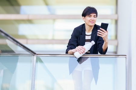 Smiling woman using smartphone on balcony in office