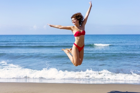 Happy woman in bikini jumping in air on beach