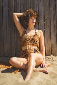 Relaxed woman sitting on sand touching curly hair