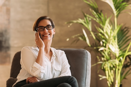 Smiling businesswoman in eyeglasses talking on mobile phone indoors