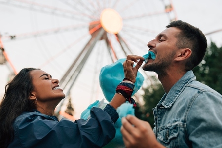 Laughing girlfriend feeding her boyfriend with cotton candy  Young couple having fun in amusement park eat cotton candy