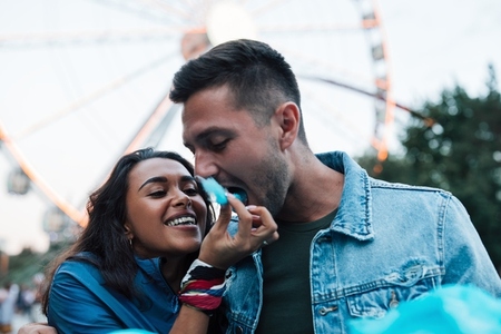 Young couple eats cotton candy during the festival  Cheerful girlfriend feeds her boyfriend with blue cotton candy