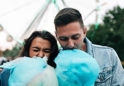 Close up of a young couple biting blue cotton candy in an amusement park