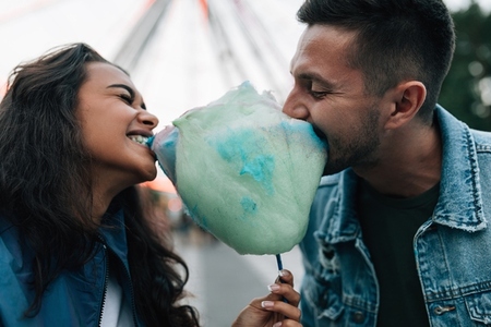 Man and woman biting cotton candy and having fun during festival