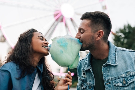 Young guys are having fun in an amusement park  Girlfriend and her boyfriend biting cotton candy during the festival