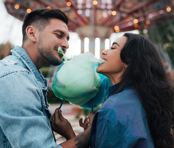 Young happy couple biting cotton candy  Man and his girlfriend bite a blue cotton candy against the carousel