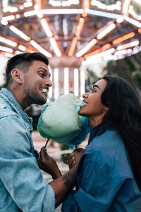 Side view of a boyfriend and girlfriend having fun and biting cotton candy