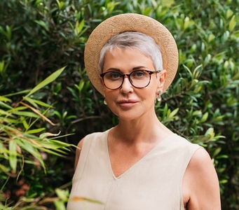 Senior woman with short grey hair  glasses  and straw hat looking at camera in a park