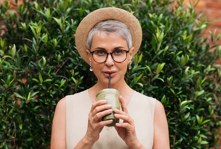 Stylish mature woman with grey hair drinking matcha latte outdoors