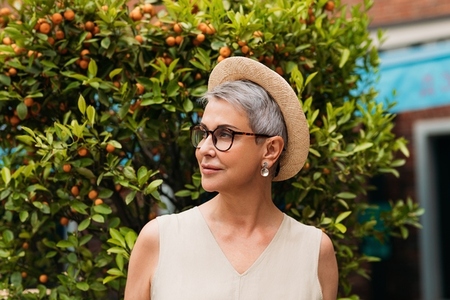 Stylish mature female wearing a small straw hat and eyeglasses looking away