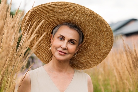 Portrait of an aged woman in a straw hat looking at the camera while standing on the field