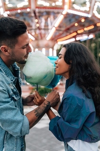 Young couple biting cotton candy during a date in an amusement park