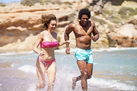 Happy diverse couple sprinting in seawater and enjoying