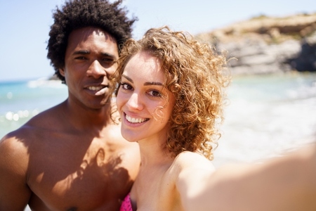 Selfie of happy diverse couple on beach