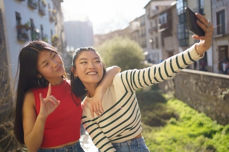 Young Asian female friends taking self portrait on cellphone during sightseeing
