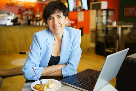 Smiling mature woman with food working on laptop in cafe