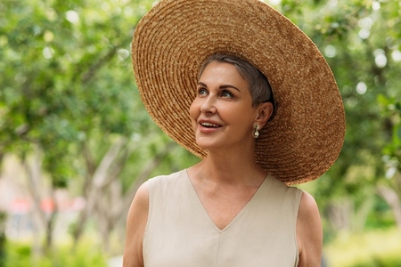 Happy senior female in a straw hat looking up while standing in a park