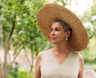 Portrait of an aged woman in a straw hat standing in the park at summer