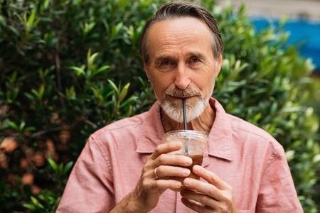 Senior man drinking a smoothie and looking at camera while standing on the park