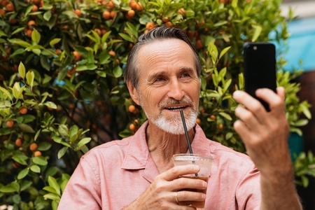 Smiling senior male taking selfie while drinking a smoothie in the park