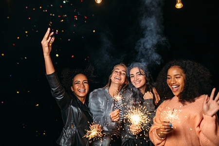 Four diverse women having fun outdoors holding sparklers and throwing confetti