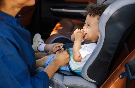 Little smiling boy laughing while sitting in baby safety car seat