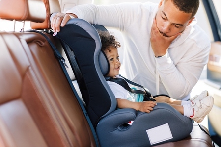 Side view of a little cute boy in a car sitting in a baby safety seat