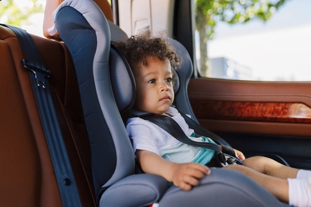 Side view of a little cute boy sitting in a baby safety car seat
