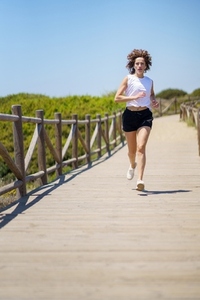Confident sportswoman jogging on wooden path
