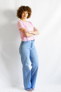Full body of woman with curly hair standing against white wall crossing arms