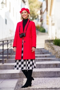 Stylish woman in red coat standing on city street in sunlight