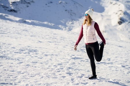 Young sporty woman standing on one leg on snowy terrain