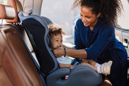 Happy mother adjusting belt on a baby car seat  Little boy smiling while his mother prepared his car seat for the trip
