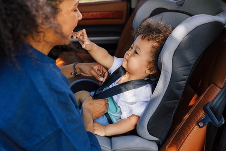 Little boy playing with her mother while she adjusting the belts on his car seat