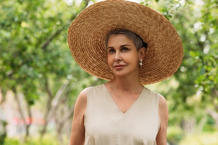 Portrait of an aged female in a big straw hat looking away while standing outdoors