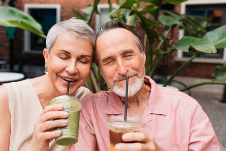 Aged smiling couple enjoying smoothies outdoors  Senior couple drinking cocktails together with closed eyes