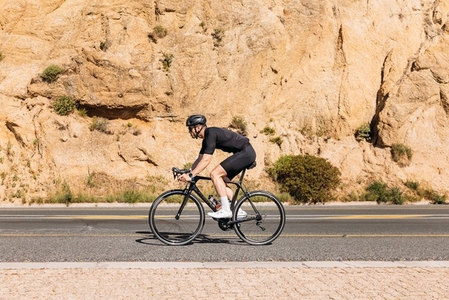 Side view of a professional cyclist in black sportswear riding bike at mountain