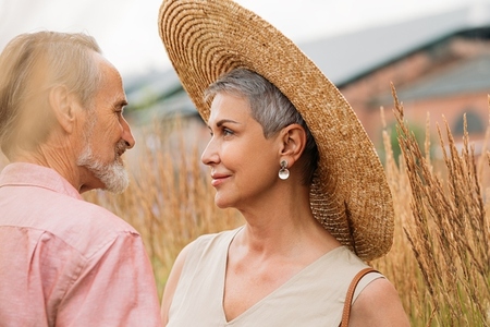 Aged woman with short gray hair wearing a straw hat looking at her husband