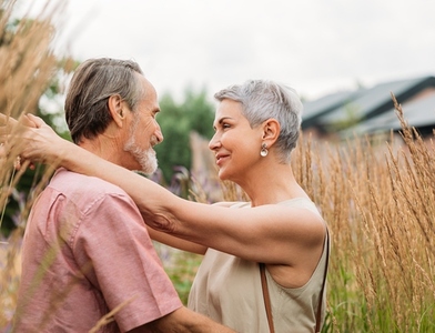 Aged people hugging and looking at each other while standing on a wheat field