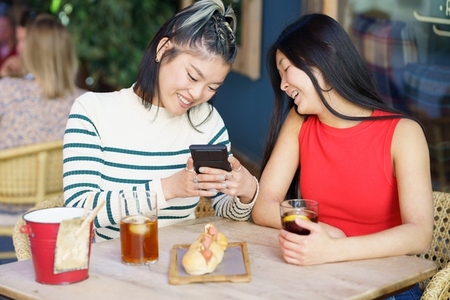 Cheerful Asian women taking picture of yummy food in cafe