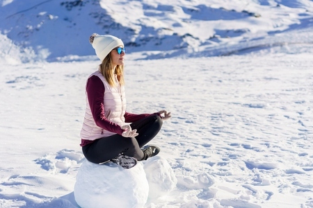 Serious woman in warm clothes sitting on snow in lotus pose