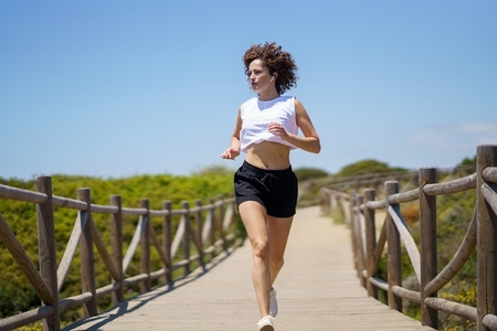 Sportswoman running along wooden path on sunny day