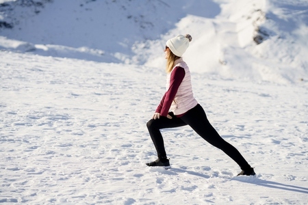 Woman stretching legs in snowy terrain