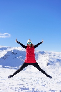 Carefree young woman jumping with raised arms in snowy terrain
